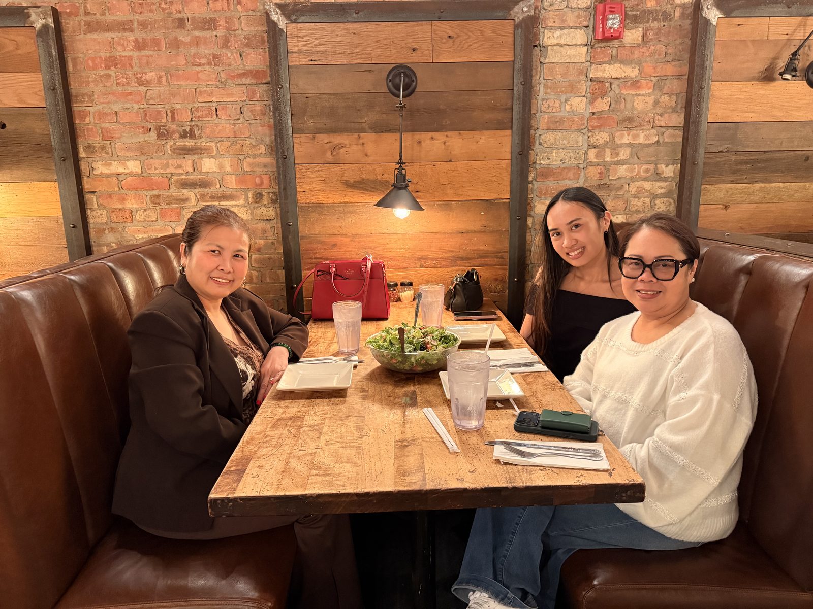 Genalyn and two young women sharing a meal at a wooden restaurant table