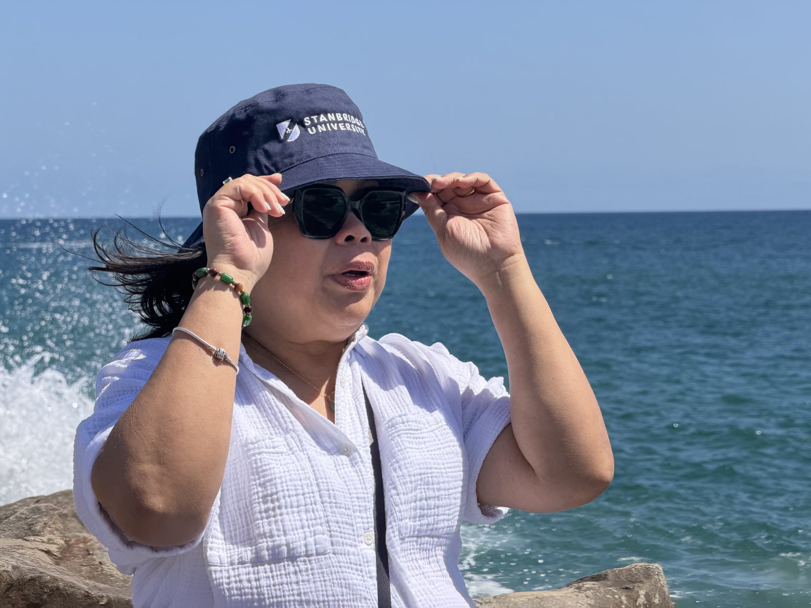 Genalyn by the sea, holding the brim of her hat in the wind